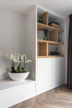 a white bowl with flowers in it sitting on a shelf next to a black curtain