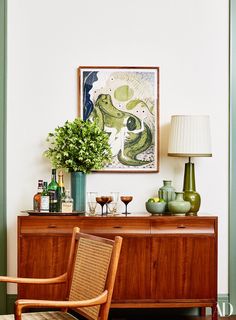 a living room with a painting on the wall next to a wooden dresser and chair