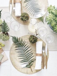 the table is set with plates, silverware and green plants