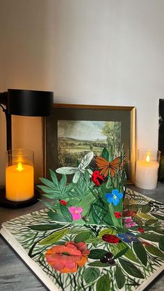 two lit candles sitting on top of a table next to some pictures and flowers in front of them