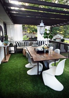 an outdoor living area with white chairs and a wooden table on the grass covered deck