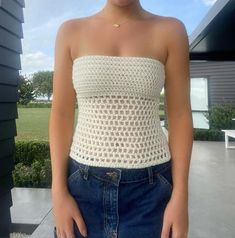 a woman wearing a white crochet top standing in front of a house