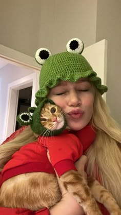 a woman holding a cat in her arms wearing a frog hat with eyes on it