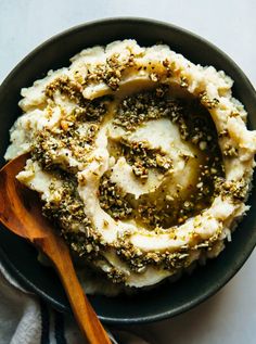 a bowl filled with mashed potatoes covered in seasoning next to a wooden spoon