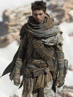 a young man dressed in armor standing on top of a snow covered mountain with his hands in his pockets