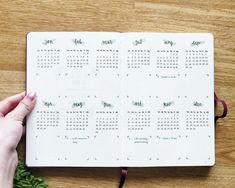 a person holding a pen and looking at a calendar on a desk with plants around it