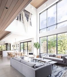 a living room filled with lots of furniture next to large windows on top of a wooden ceiling