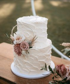 a wedding cake sitting on top of a wooden table next to pink flowers and greenery