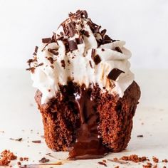 a chocolate cupcake with whipped cream and chocolate shavings on the top is half eaten