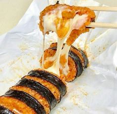 several pieces of sushi being lifted by chopsticks with cheese and sauce on them