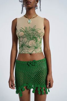 a woman in a crop top and green crochet skirt with flowers on it