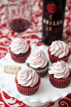 cupcakes with white frosting on a red and white tablecloth next to a bottle of wine