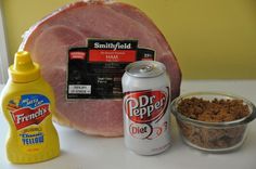 ham, mustard, and other ingredients are sitting on a counter top next to a can of soda