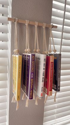 a row of books hanging from the side of a wall next to a window with white blinds