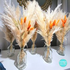 three glass vases with dried flowers in them on a white countertop next to a mirror