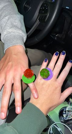 two people with their hands on the steering wheel of a car, one holding a gummy bear