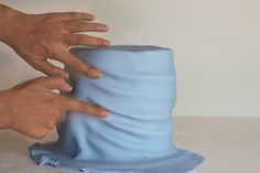 two hands reaching for a blue hat on a white surface with one hand touching the top