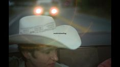 a man wearing a white cowboy hat while sitting in the back seat of a car