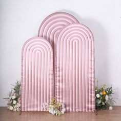 three pink arches with flowers on the floor in front of white wall and wooden table