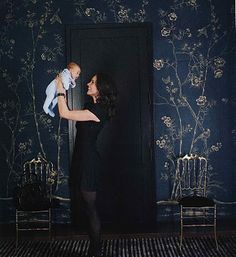 a woman holding a baby in front of a blue wall with gold flowers on it