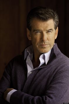 a man with his arms crossed looking at the camera while wearing a purple sweater and white shirt