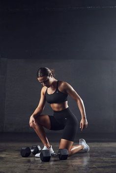 a woman squatting down with two dumbbells in front of her on the ground