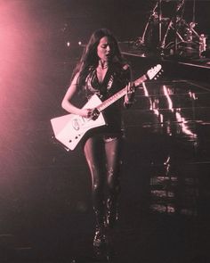 a woman holding a guitar while standing on stage