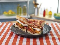 a plate with a sandwich cut in half on top of a red and white table cloth