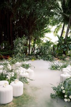 an outdoor ceremony setup with white flowers and greenery on the ground, surrounded by tall trees