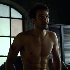 a shirtless man standing next to a window in the dark with his hands on his hips