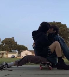 two people sitting on the ground with skateboards in front of them and one person kissing the other