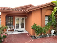 an orange house with potted plants and a white bench in front of the door