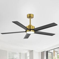 a ceiling fan in a living room with white walls and large windows, gold trim on the blades