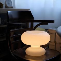 an illuminated table lamp sitting on top of a wooden table next to a black chair