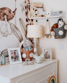 a white dresser topped with pictures and stuffed animals next to a wall mounted giraffe