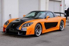 an orange and black sports car parked in front of a garage with two doors open