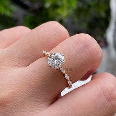 a woman's hand with a diamond ring on top of her finger, in front of some plants