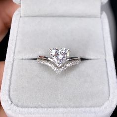 a person holding a ring with a heart shaped diamond on it's side in a box