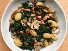 a white bowl filled with mushrooms and spinach on top of a wooden table next to a fork