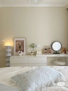 a white bed sitting under a chandelier next to a mirror and table with vases on it