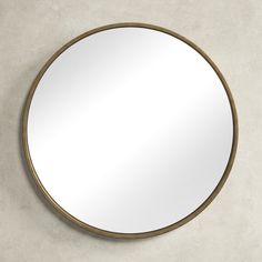 a round mirror mounted on the wall above a concrete counter top with an aged brass frame