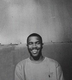 a black and white photo of a smiling man in front of a wall with no one on it