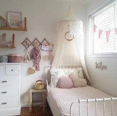 a white bed sitting under a window next to a dresser and shelf in a bedroom