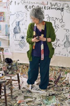 an older woman standing in front of a pile of paper and looking at her cell phone