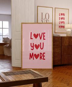 a pink poster with the words love you more on it in front of a wooden table