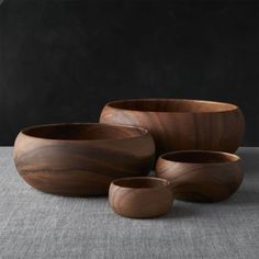 three wooden bowls sitting next to each other on a gray tableclothed surface with black walls in the background