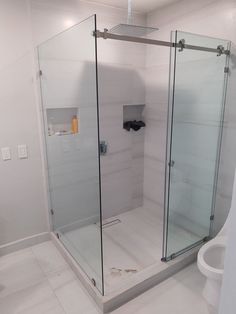 a bathroom with a glass shower stall and white tile flooring on the walls, along with a toilet in the corner