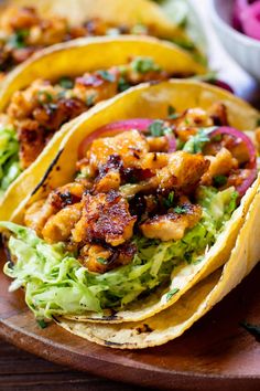 three tacos with chicken and lettuce on a wooden platter