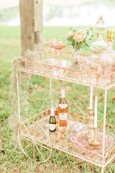 a pink bar cart with bottles and glasses on it sitting in the grass next to a tree