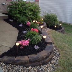 some lights are on in the middle of a flower bed with rocks and flowers around it